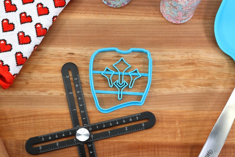 May include: A blue plastic cookie cutter shaped like a tooth with a design of three stylized flowers inside. The cutter is on a wooden surface.