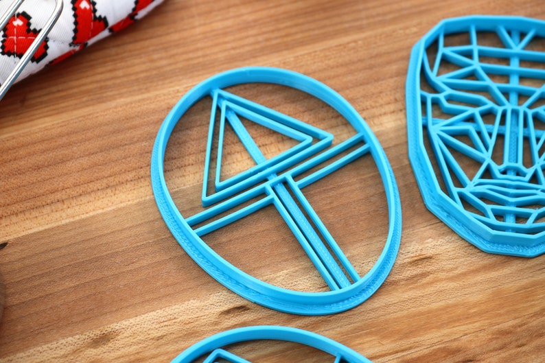 May include: Three blue plastic cookie cutters, one shaped like a circle with a triangle and lines inside, one shaped like a circle with a triangle inside, and one shaped like a face.