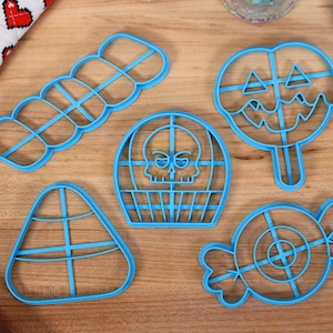 May include: Five blue plastic cookie cutters shaped like a skull, a lollipop, a candy cane, a candy, and a row of five circles.