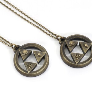 Puede incluir: Dos collares de color dorado con colgantes que representan el s&iacute;mbolo Triforce de la serie de videojuegos The Legend of Zelda. Cada colgante tiene un dise&ntilde;o circular con un s&iacute;mbolo Triforce en relieve en el centro.