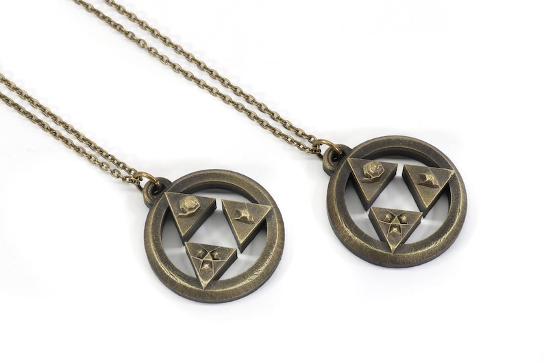 Puede incluir: Dos collares de color dorado con colgantes que representan el s&iacute;mbolo Triforce de la serie de videojuegos The Legend of Zelda. Cada colgante tiene un dise&ntilde;o circular con un s&iacute;mbolo Triforce en relieve en el centro.