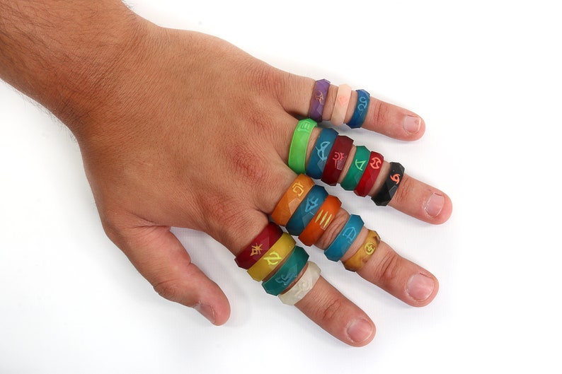 May include: A hand wearing a variety of colorful silicone rings with different symbols and designs. The rings are stacked on each finger.