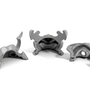 May include: Three gray plastic pieces of a 3D printed helmet with horns. The helmet is disassembled and the pieces are laying on a white surface.