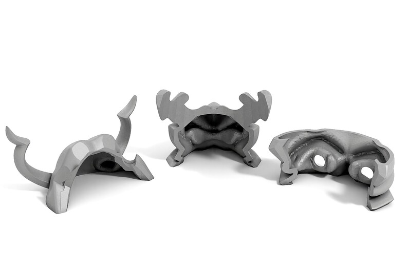 May include: Three gray plastic pieces of a 3D printed helmet with horns. The helmet is disassembled and the pieces are laying on a white surface.