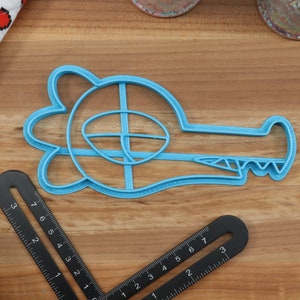 May include: A blue plastic cookie cutter shaped like an alligator with an open mouth and teeth. The cutter has a detailed design with a raised eye and a textured body.