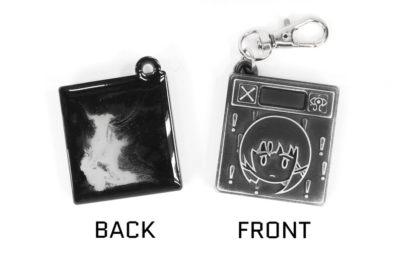 May include: A black and silver metal keychain with a cartoon character on the front and a blank surface on the back. The keychain features a small, silver, metal loop for attaching to a bag or keys.