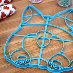 May include: A blue plastic cookie cutter shaped like a cartoon dog. The cutter has a heart-shaped nose and paw prints on the bottom.