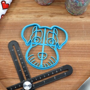 May include: A blue plastic cookie cutter shaped like a dog's head. The cutter has detailed features, including eyes, a nose, and a mouth.