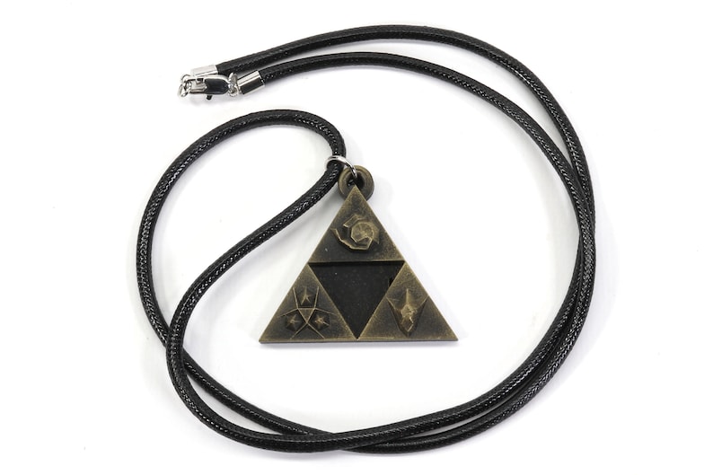 May include: A black cord necklace with a gold-toned pendant featuring a triangular design with symbols. The pendant is a stylized representation of the Triforce from the Legend of Zelda video game series.