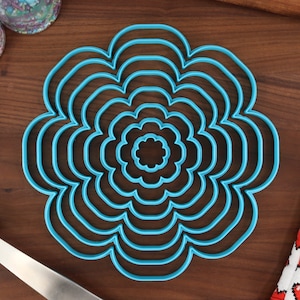May include: A set of eight blue plastic flower-shaped cookie cutters of varying sizes. The cutters are arranged in a circle, with the smallest cutter in the center.