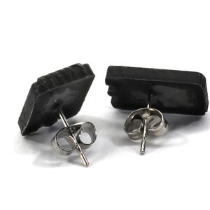 May include: A pair of black stud earrings with silver posts. The earrings are shaped like small rectangles.