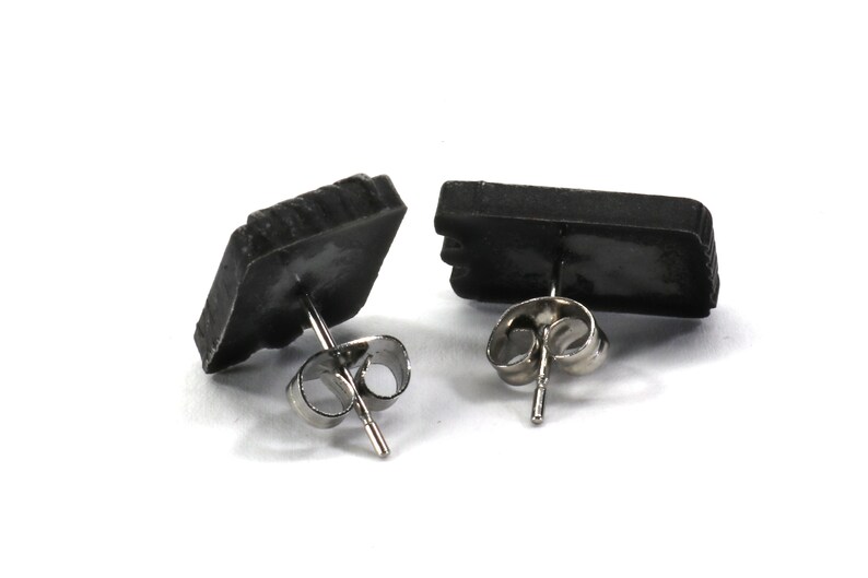 May include: A pair of black stud earrings with silver posts. The earrings are shaped like small rectangles.
