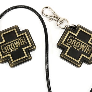 May include: A black lanyard with a silver clasp and two black and gold metal cross charms. Each charm has the word "GROWTH" written on it.