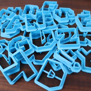 May include: A set of blue plastic cookie cutters in various geometric shapes. The cutters are arranged in a pile on a wooden surface.