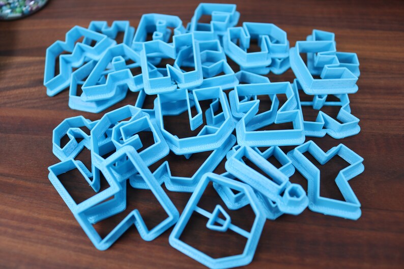 May include: A set of blue plastic cookie cutters in various geometric shapes. The cutters are arranged in a pile on a wooden surface.