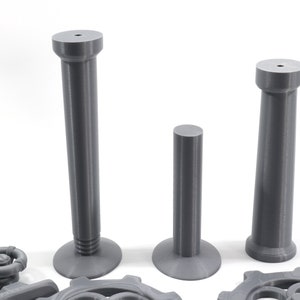 May include: Three gray plastic columns of varying heights. The columns have a smooth, cylindrical shape with a slightly flared base. The columns are arranged in a row from tallest to shortest.