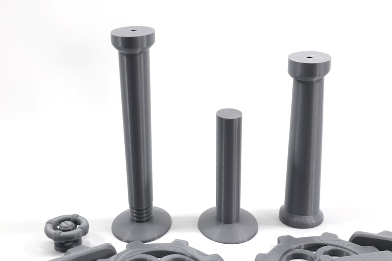 May include: Three gray plastic columns of varying heights. The columns have a smooth, cylindrical shape with a slightly flared base. The columns are arranged in a row from tallest to shortest.