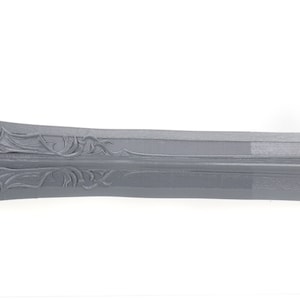 Puede incluir: Primer plano de una espada de metal gris con tallas intrincadas en la hoja.