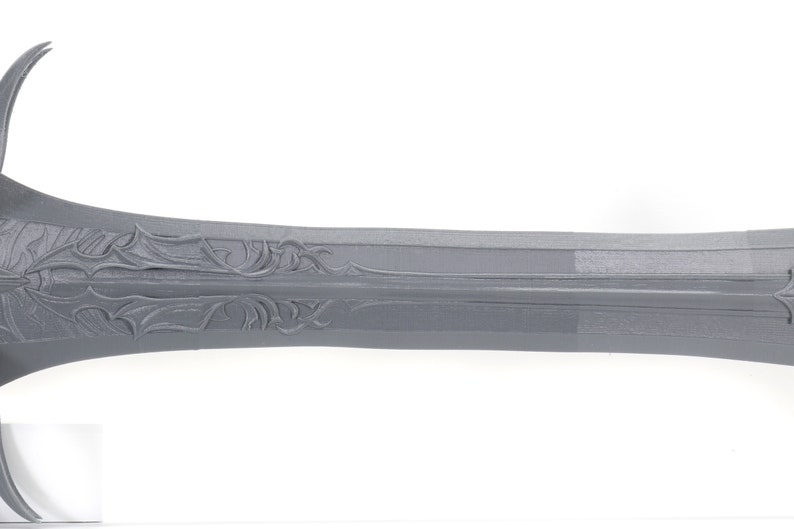 Puede incluir: Primer plano de una espada de metal gris con tallas intrincadas en la hoja.
