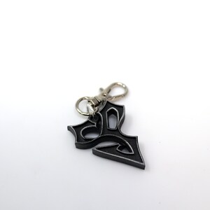 May include: A black metal keychain with a decorative design. The keychain has a silver metal loop.