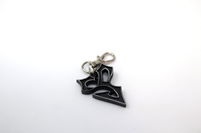 May include: A black metal keychain with a decorative design. The keychain has a silver metal loop.
