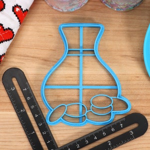 May include: Blue plastic cookie cutter shaped like a vase with a grid pattern and a row of circles at the bottom.