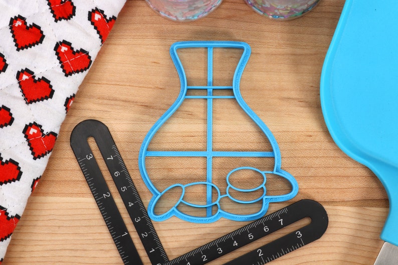 May include: Blue plastic cookie cutter shaped like a vase with a grid pattern and a row of circles at the bottom.
