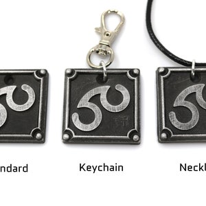 May include: Three versions of a silver and black metal pendant featuring a stylized symbol. The pendant is available as a standard piece, a keychain, and a necklace.