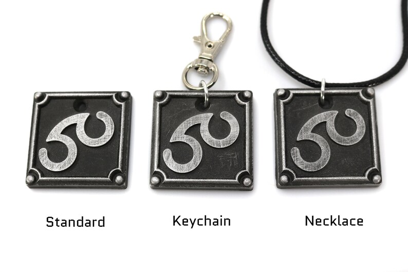 May include: Three versions of a silver and black metal pendant featuring a stylized symbol. The pendant is available as a standard piece, a keychain, and a necklace.