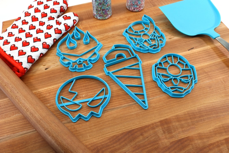 May include: A set of six blue plastic cookie cutters shaped like a skull with flames, a drill, a skull with a lightning bolt, and two different faces. The cutters are on a wooden surface.