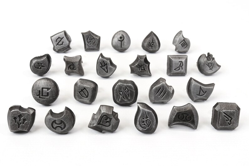 Puede incluir: Una colecci&oacute;n de veinticuatro objetos grises, similares a piedras, con s&iacute;mbolos grabados. Los objetos var&iacute;an en forma, incluyendo formas geom&eacute;tricas y org&aacute;nicas. Cada pieza presenta un dise&ntilde;o &uacute;nico grabado, sugiriendo un conjunto de piezas de juego o elementos decorativos.