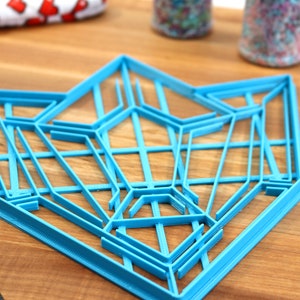 Puede incluir: Un cortador de galletas geom&eacute;trico de pl&aacute;stico azul en forma de estrella. El cortador est&aacute; sobre una superficie de madera.