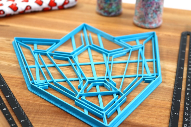 Puede incluir: Un cortador de galletas geom&eacute;trico de pl&aacute;stico azul en forma de estrella. El cortador est&aacute; sobre una superficie de madera.