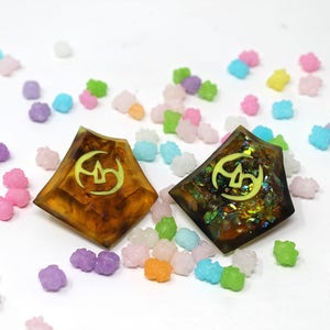 May include: Two resin dice with a yellow symbol on a white background surrounded by colorful candy.