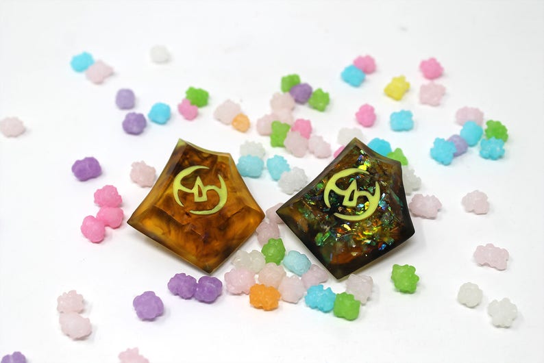 May include: Two resin dice with a yellow symbol on a white background surrounded by colorful candy.