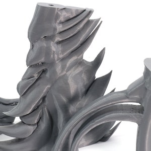 May include: A 3D printed gray sculpture with a face-like design and sharp, pointed edges. The sculpture is made of plastic and has a smooth, matte finish.