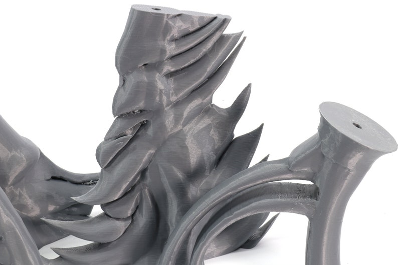 May include: A 3D printed gray sculpture with a face-like design and sharp, pointed edges. The sculpture is made of plastic and has a smooth, matte finish.