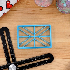 May include: A blue plastic cookie cutter shaped like a Union Jack flag on a wooden surface.