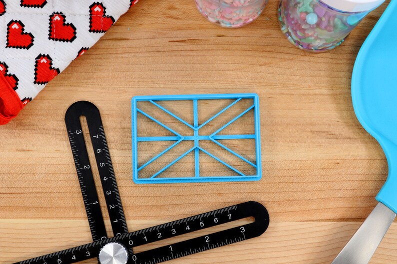 May include: A blue plastic cookie cutter shaped like a Union Jack flag on a wooden surface.