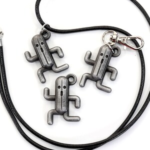 May include: Three silver-colored charm pendants shaped like a running character from a video game, hanging from a black cord with a silver clasp.