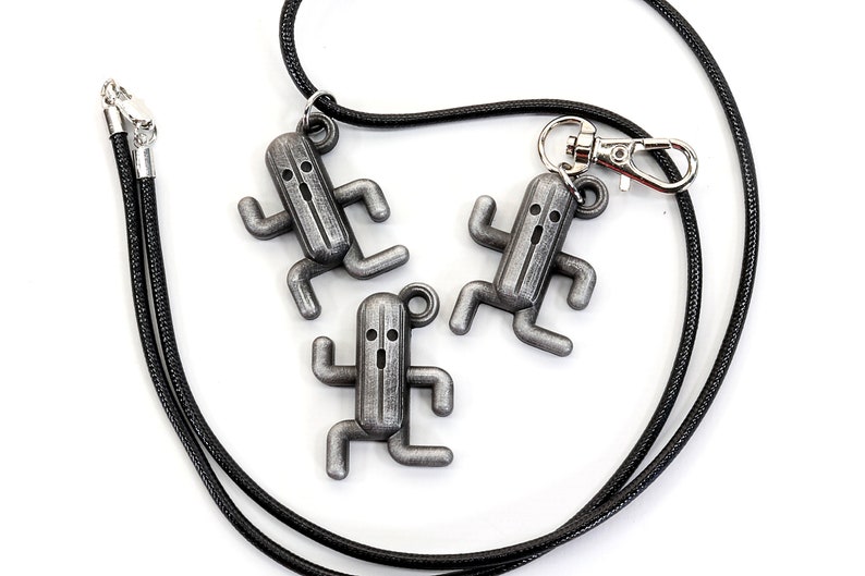 May include: Three silver-colored charm pendants shaped like a running character from a video game, hanging from a black cord with a silver clasp.