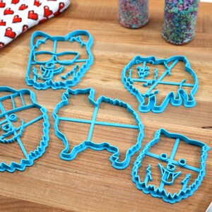 May include: Five blue plastic cookie cutters shaped like dogs. The cutters have different expressions, including sunglasses, a hat, and a tongue sticking out.