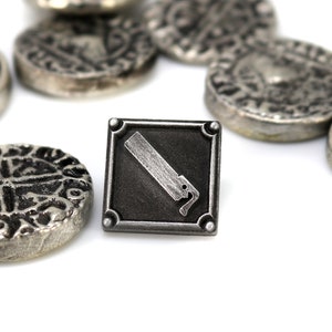 May include: A silver metal pin with a black square background and a silver saw blade design. The pin is surrounded by several silver metal coins with intricate designs.