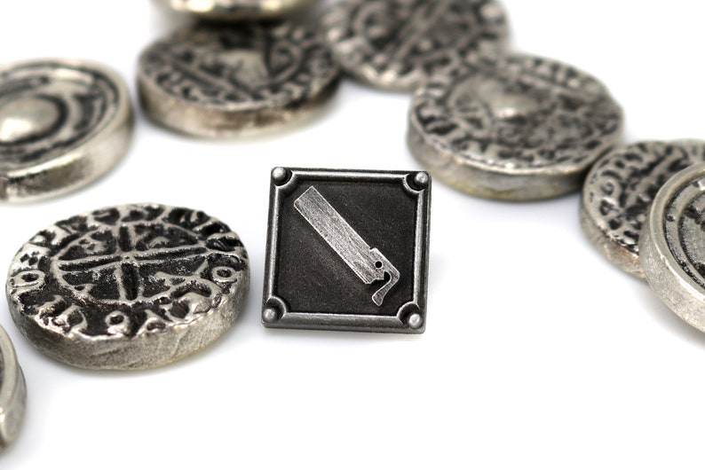 May include: A silver metal pin with a black square background and a silver saw blade design. The pin is surrounded by several silver metal coins with intricate designs.