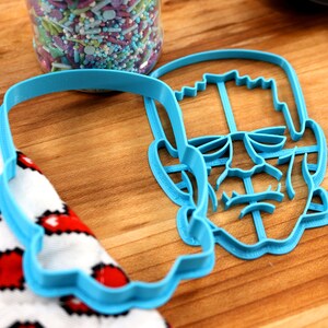 May include: Blue plastic cookie cutter shaped like Frankenstein's face. The cutter has detailed features including eyes, nose, mouth, and neck bolts.