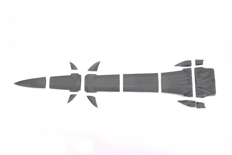 May include: A gray plastic model kit of a futuristic spaceship, disassembled into multiple pieces. The pieces are laid out on a white surface.