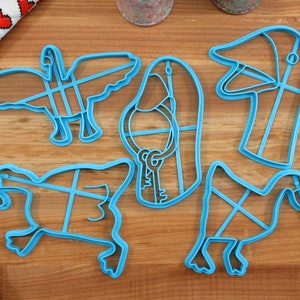 May include: A set of five blue plastic cookie cutters shaped like geese. The cutters are on a wooden surface.