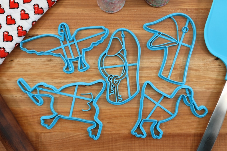 May include: A set of five blue plastic cookie cutters shaped like geese. The cutters are on a wooden surface.