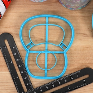 May include: A blue plastic cookie cutter shaped like a donut with a hole in the center and a decorative design around the edge.