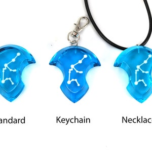 May include: Three versions of a blue pendant with a white constellation design. The pendant is available as a standard piece, a keychain, and a necklace.